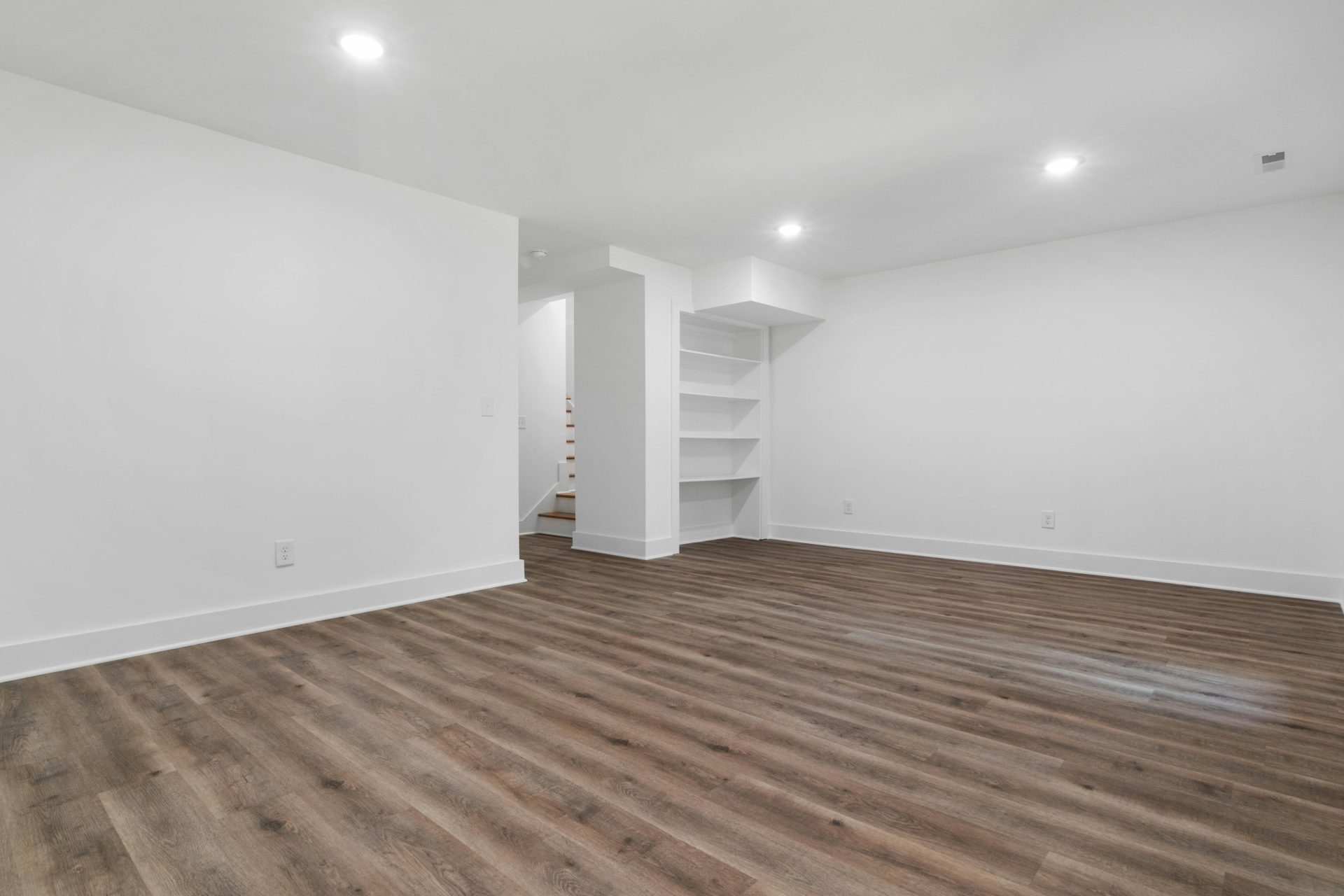 Una habitación moderna, espaciosa y minimalista, con paredes blancas, suelo de parqué y estanterías empotradas.